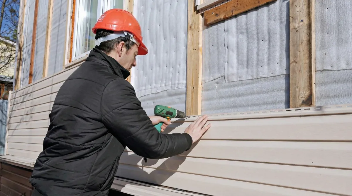 Siding replacement professional using a power drill to install new tan vinyl siding on a home exterior in Fort Collins, CO